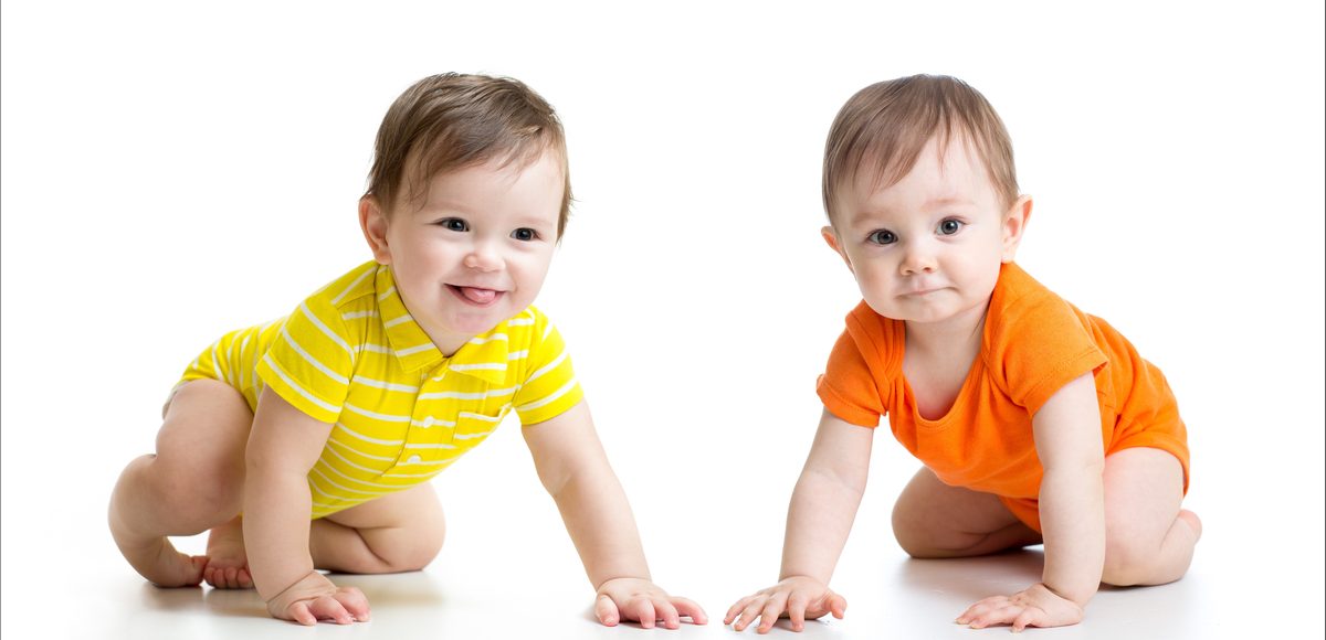 Two babies in yellow and orange shirts crawling side by side