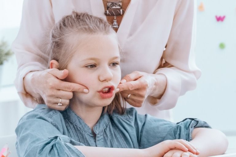 A clinician gently supporting a young girl's face during a feeding therapy exercise