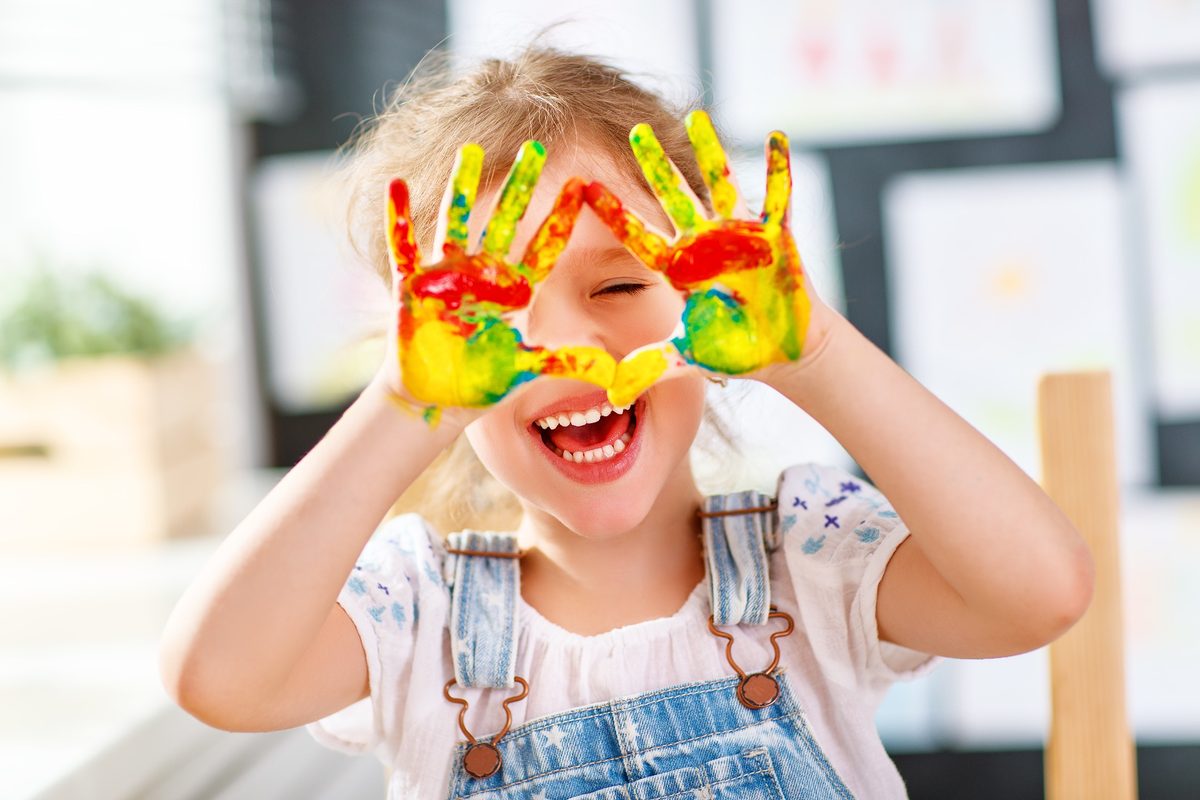 A laughing child holding up both hands covered in bright finger paint