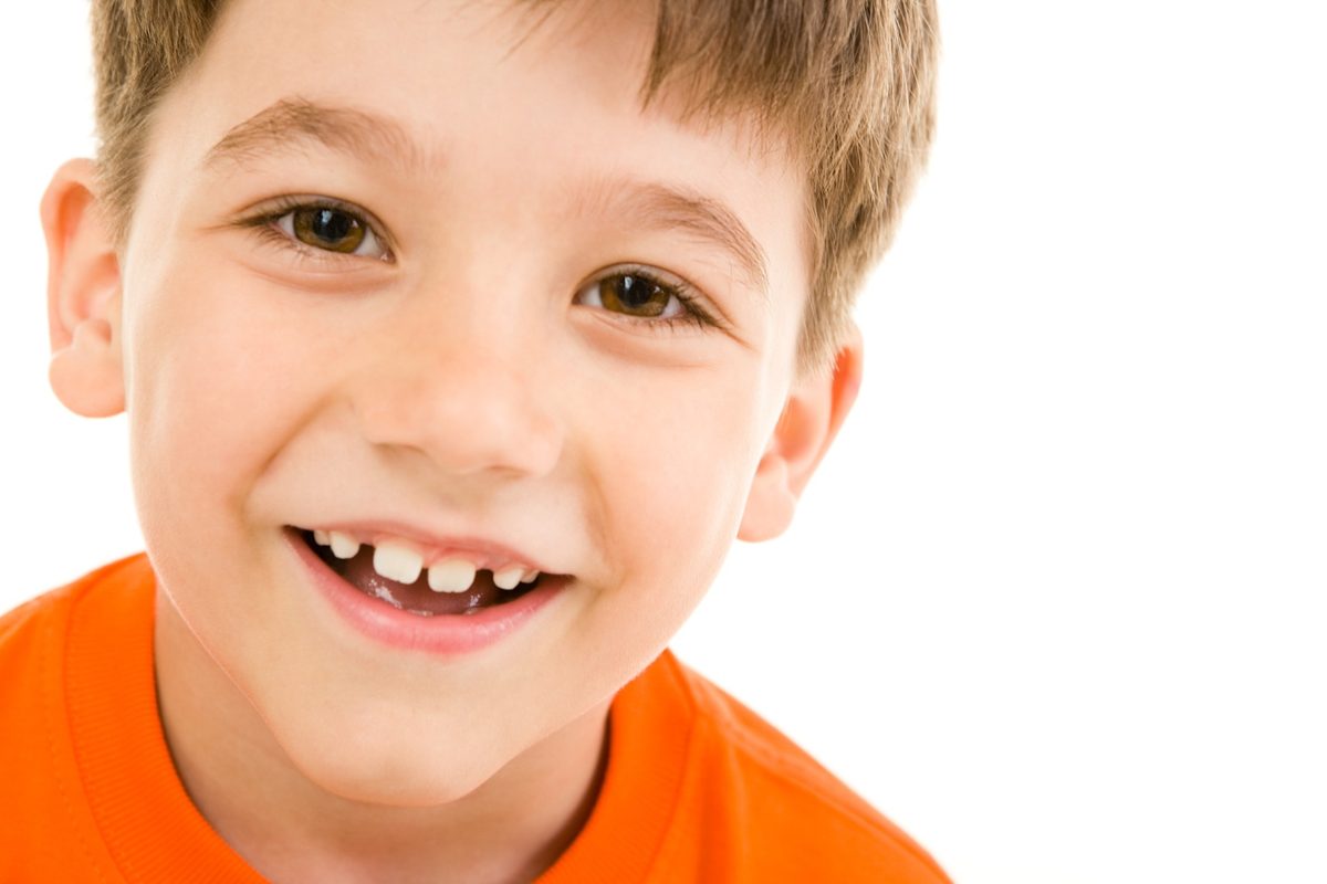 A smiling boy in an orange shirt looking directly at the camera