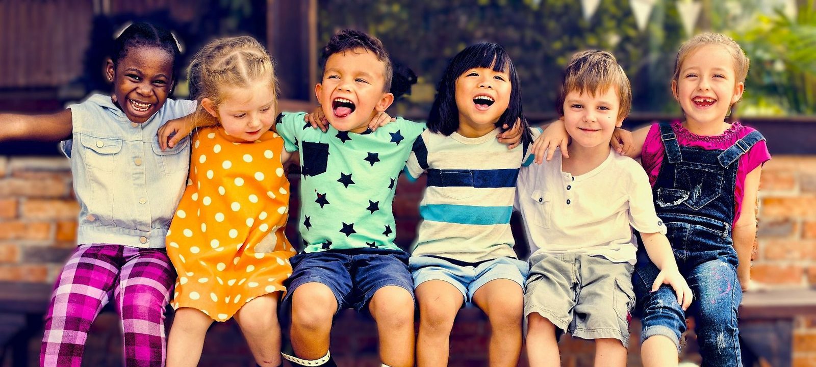 Six children of different ages sitting in a row on a bench, laughing together