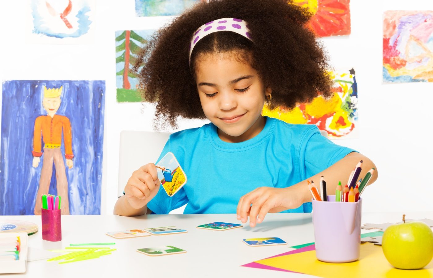 A girl at a table cutting and arranging colored paper shapes during a fine motor activity